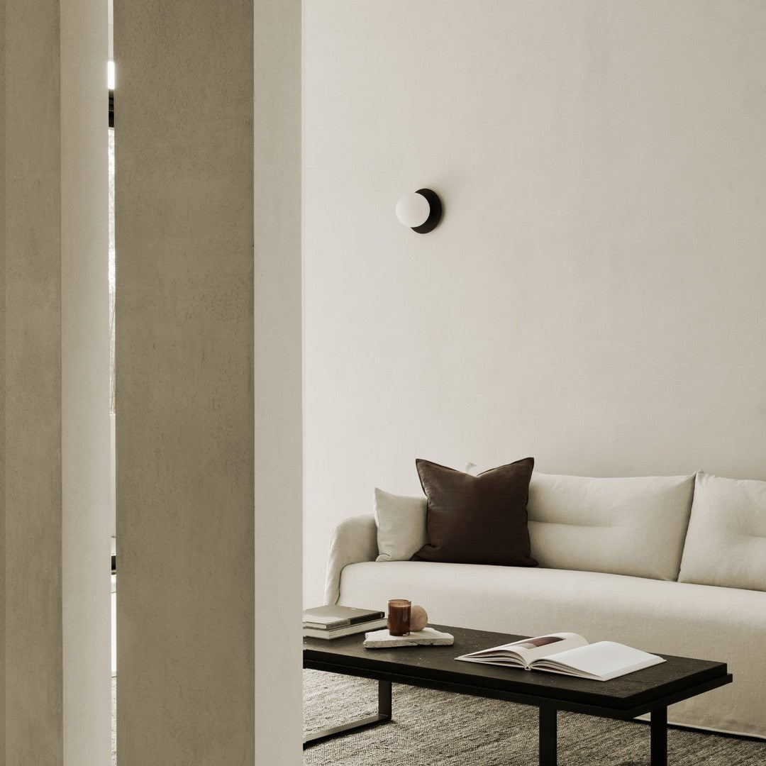 Minimalist living room featuring beige walls, a cream sofa, brown accents, and a black coffee table.