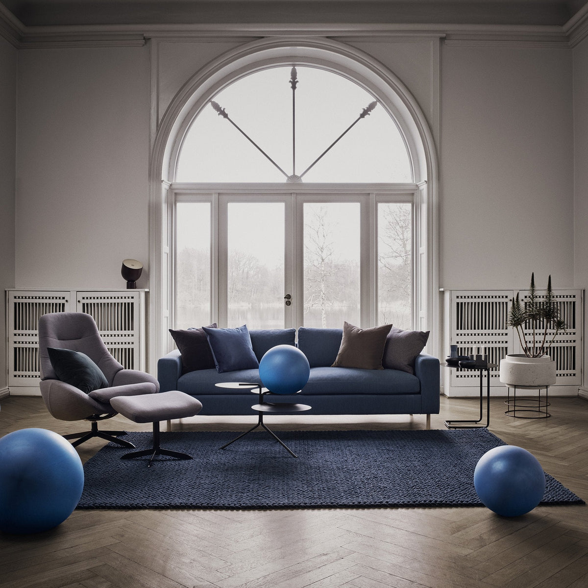 Navy blue sofa with gray and purple cushions, set on a textured navy rug, complemented by blue decorative balls.