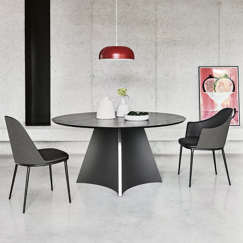 Modern round black dining table with a sleek gray base, complemented by red pendant light and patterned chairs.