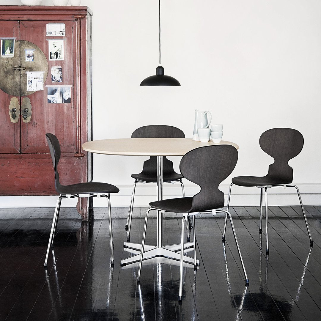 Modern black and wood dining set with a round table and stylish chairs on a dark wood floor, complemented by a sleek pendant light.