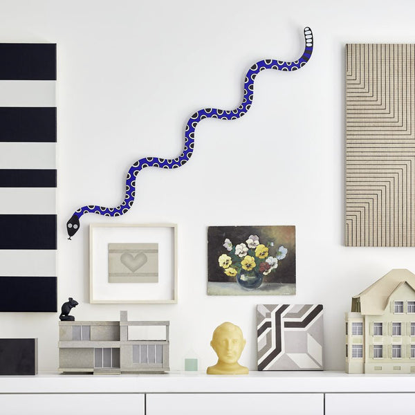 Colorful abstract snake sculpture in blue and white, set against geometric patterns in black and cream.