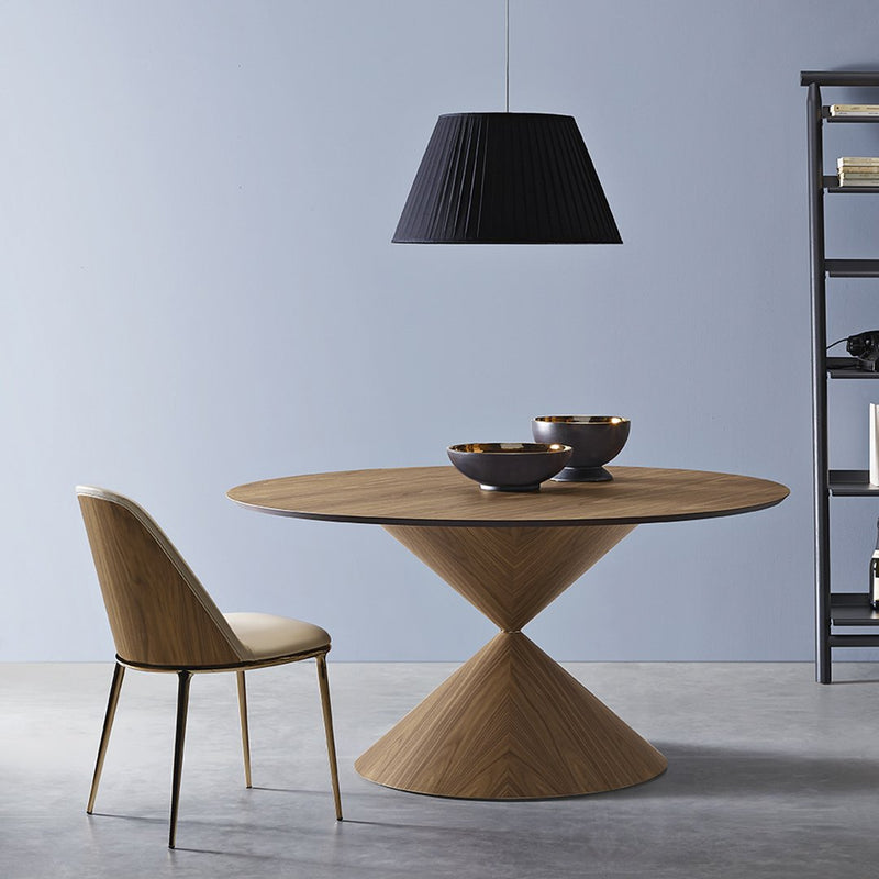 Wooden round table with a tapered base, paired with a light beige chair and black pendant lamp against a light blue wall.