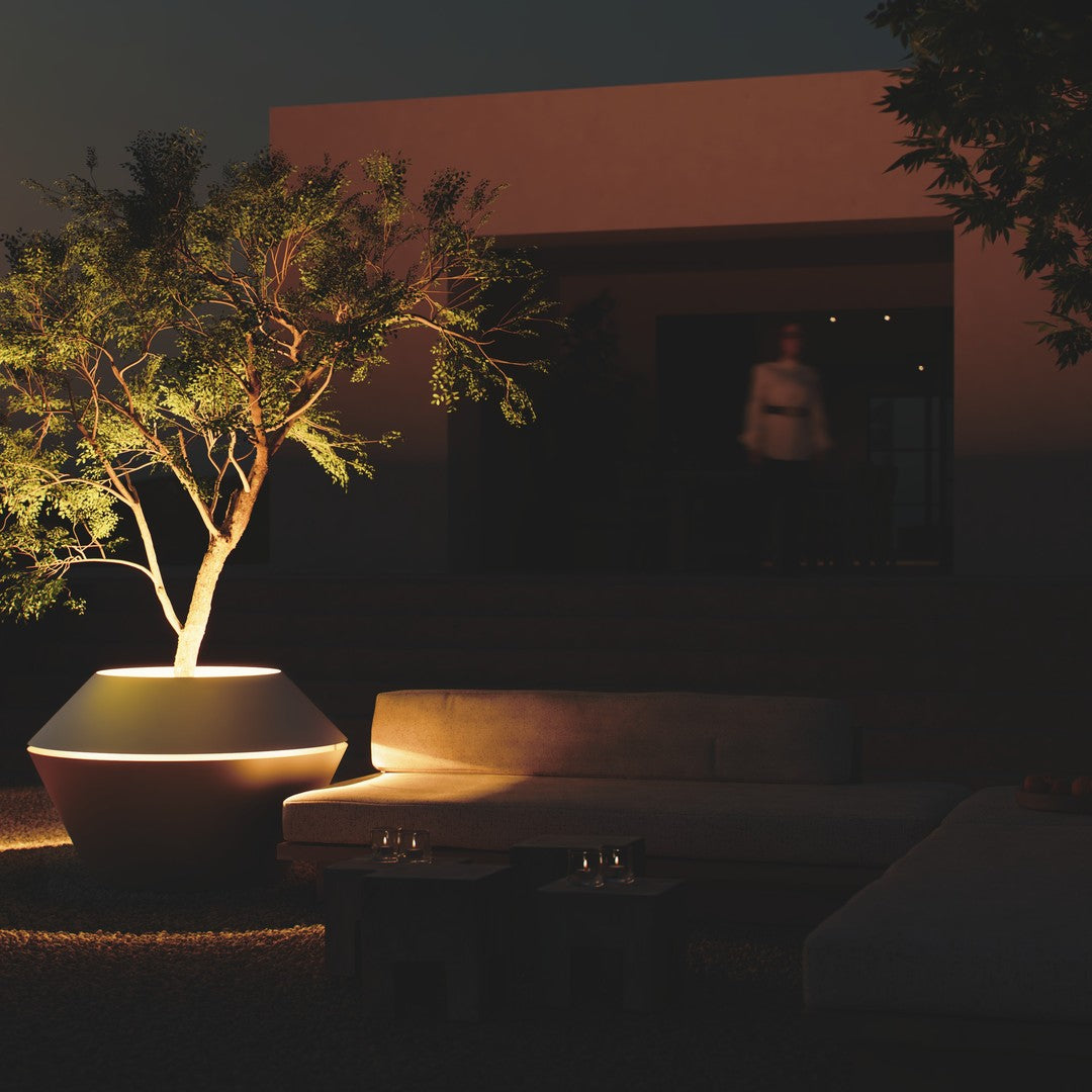 Elegant white ceramic planter with a warm glow, featuring lush green foliage against a dark, modern patio backdrop.