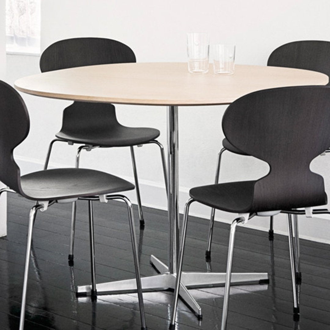 Modern round table with a light wood top and sleek chrome base, surrounded by black minimalist chairs.