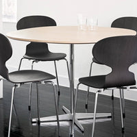 Modern round table with a light wood top and sleek chrome base, surrounded by black minimalist chairs.