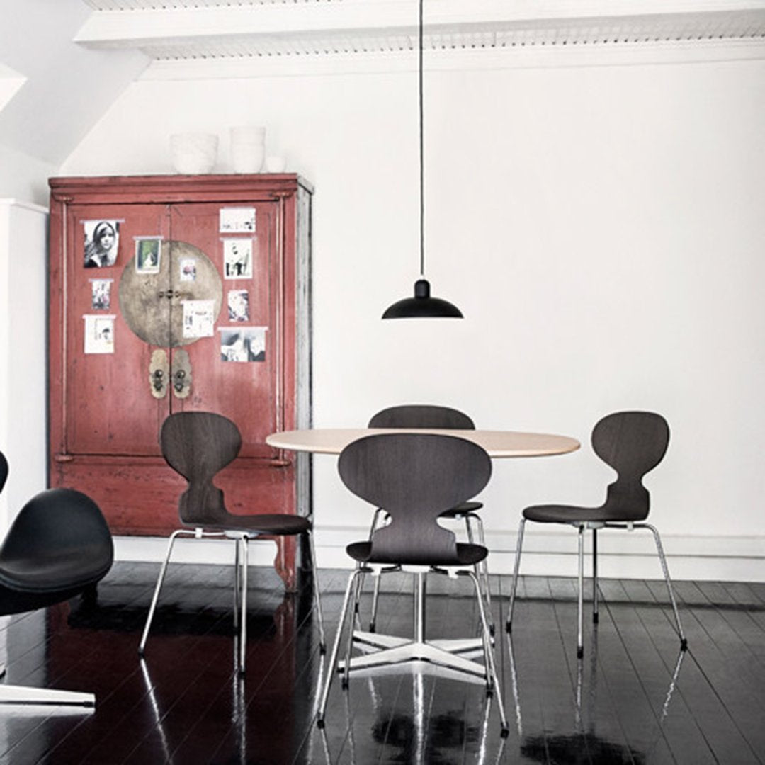 Modern dining area featuring a round wooden table, black chairs, and a deep red cabinet against white walls.