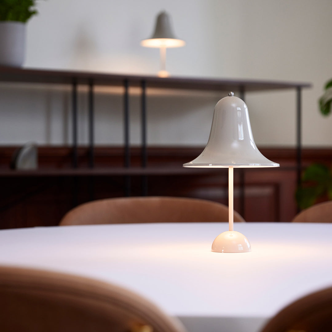 White bell-shaped lamp on a light table, soft glow, minimalist design with neutral tones. Elegant home decor piece.