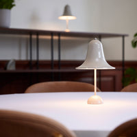 White bell-shaped lamp on a light table, soft glow, minimalist design with neutral tones. Elegant home decor piece.