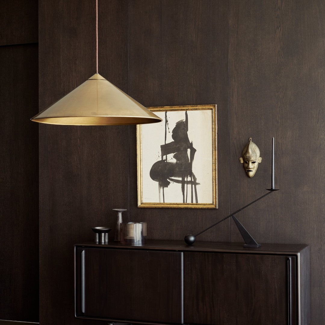 Gold conical pendant light against a dark wood wall, complemented by black and white artwork and accents.