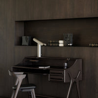 Dark wood desk with black accents, minimalist design, sleek metallic lamp, and subtle textures for a modern look.