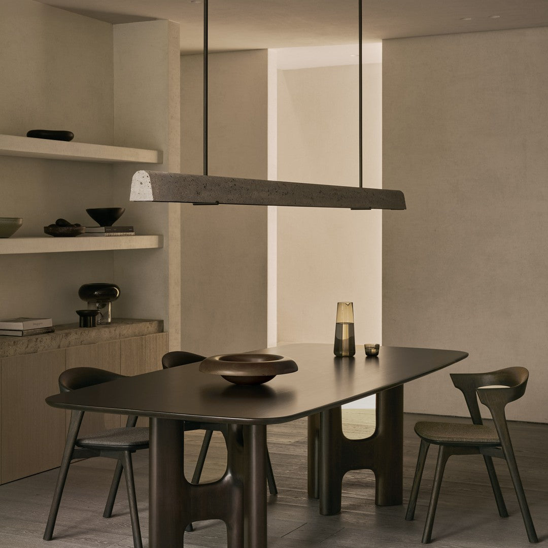 Modern minimalistic dining table with a dark, smooth finish and earthy tones, complemented by muted decor and sleek lines.