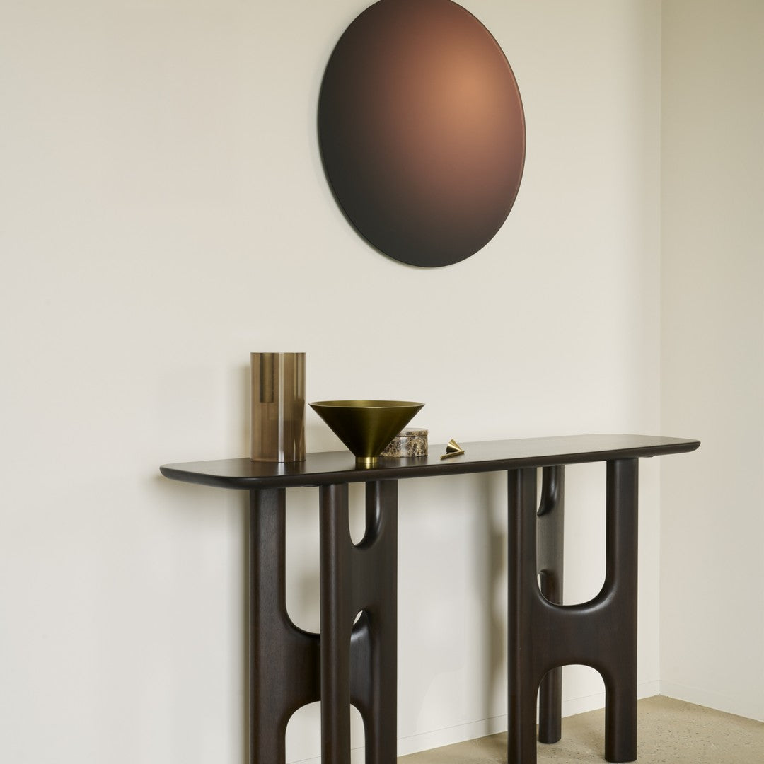 Dark wood console table with geometric cutouts, featuring a matte black wall art circle and metallic accents.