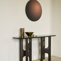 Dark wood console table with geometric cutouts, featuring a matte black wall art circle and metallic accents.