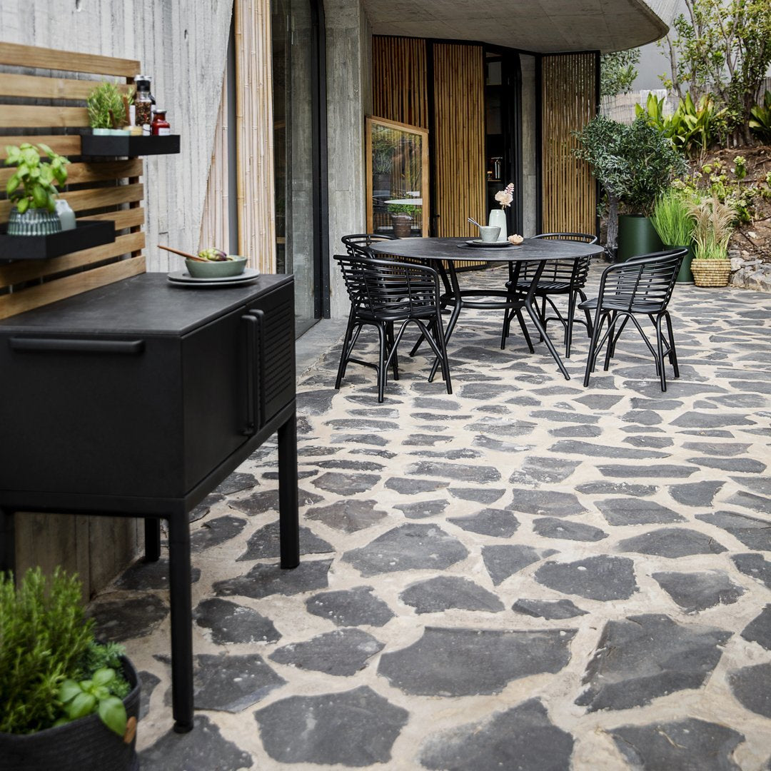 Stylish black outdoor furniture on a textured stone patio, surrounded by lush greenery and wooden accents.