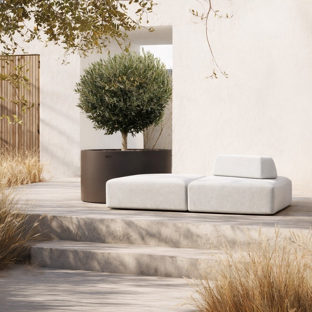 Modern outdoor sofa in soft gray fabric with minimalist design, surrounded by natural earthy tones and greenery.