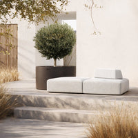 Modern outdoor sofa in soft gray fabric with minimalist design, surrounded by natural earthy tones and greenery.