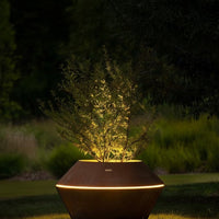 Elegant brown geometric planter with soft glowing light, featuring green foliage against a rich backdrop of nature.