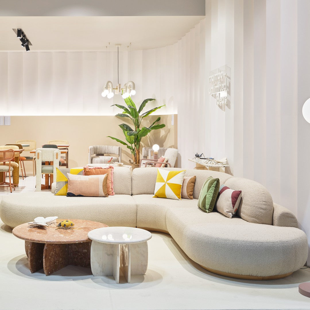 Curved beige sofa with colorful patterned pillows, complementing a modern interior design and natural greenery.