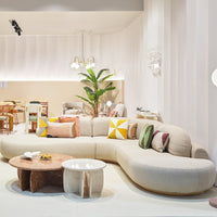 Curved beige sofa with colorful patterned pillows, complementing a modern interior design and natural greenery.