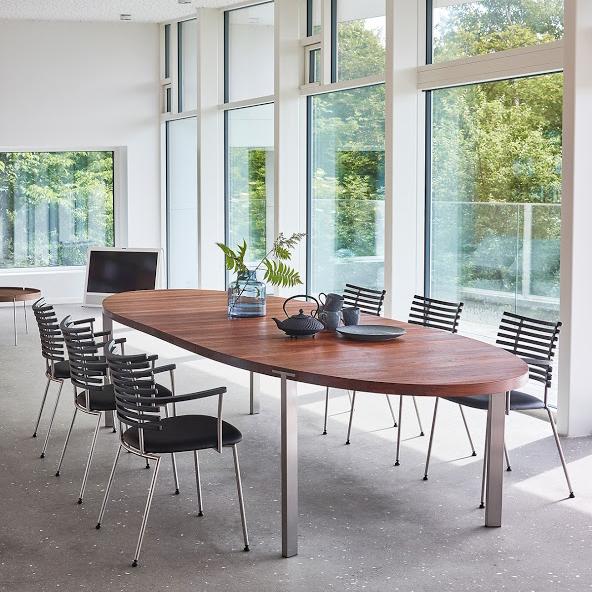 Modern wooden table with an oval shape, surrounded by sleek black and silver chairs, set in a bright, airy room.