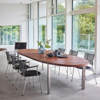 Modern wooden table with an oval shape, surrounded by sleek black and silver chairs, set in a bright, airy room.