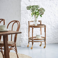 Natural rattan serving cart with a light wood finish, featuring a circular top and patterned design. White background enhances elegance.