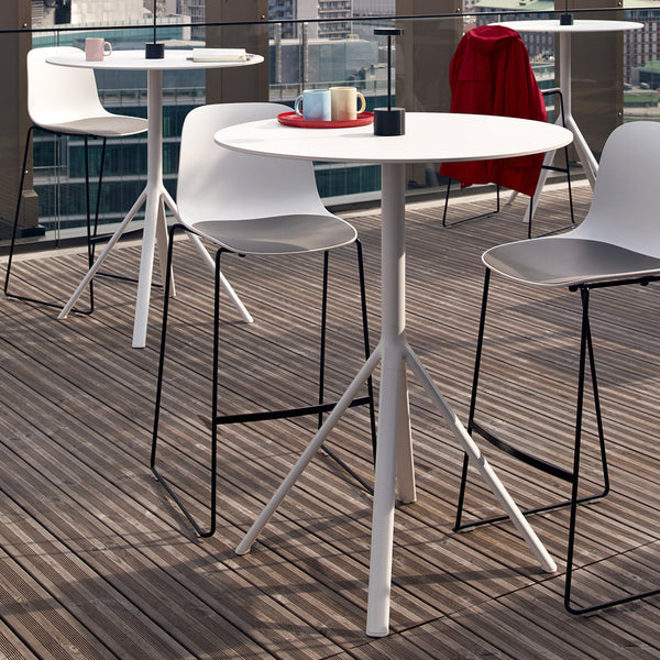 Modern outdoor table set with a sleek white round table, black and white chairs, and warm wood decking.