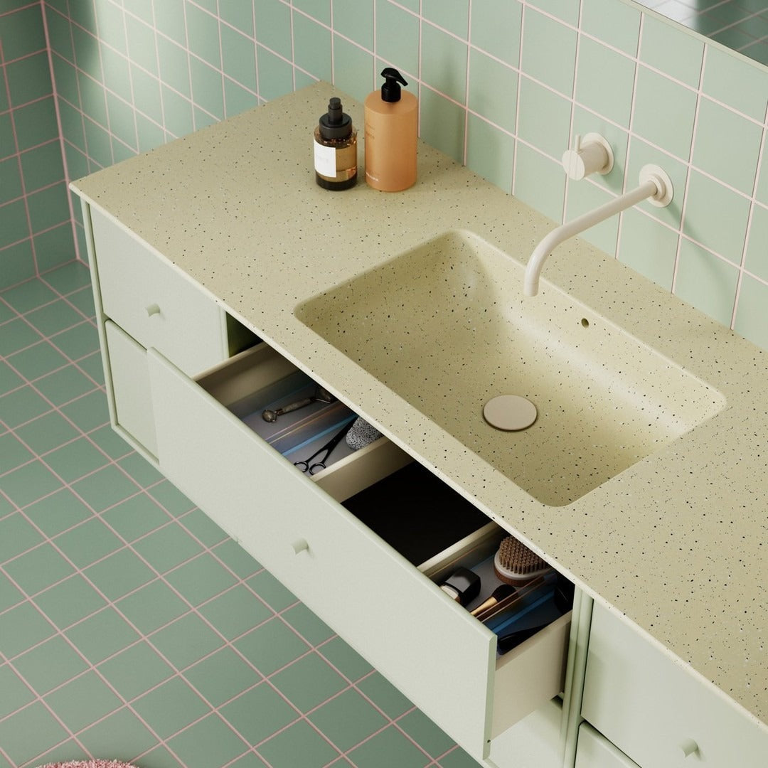 Green speckled countertop with matching mint green drawers and pastel tiled walls in a modern bathroom setting.