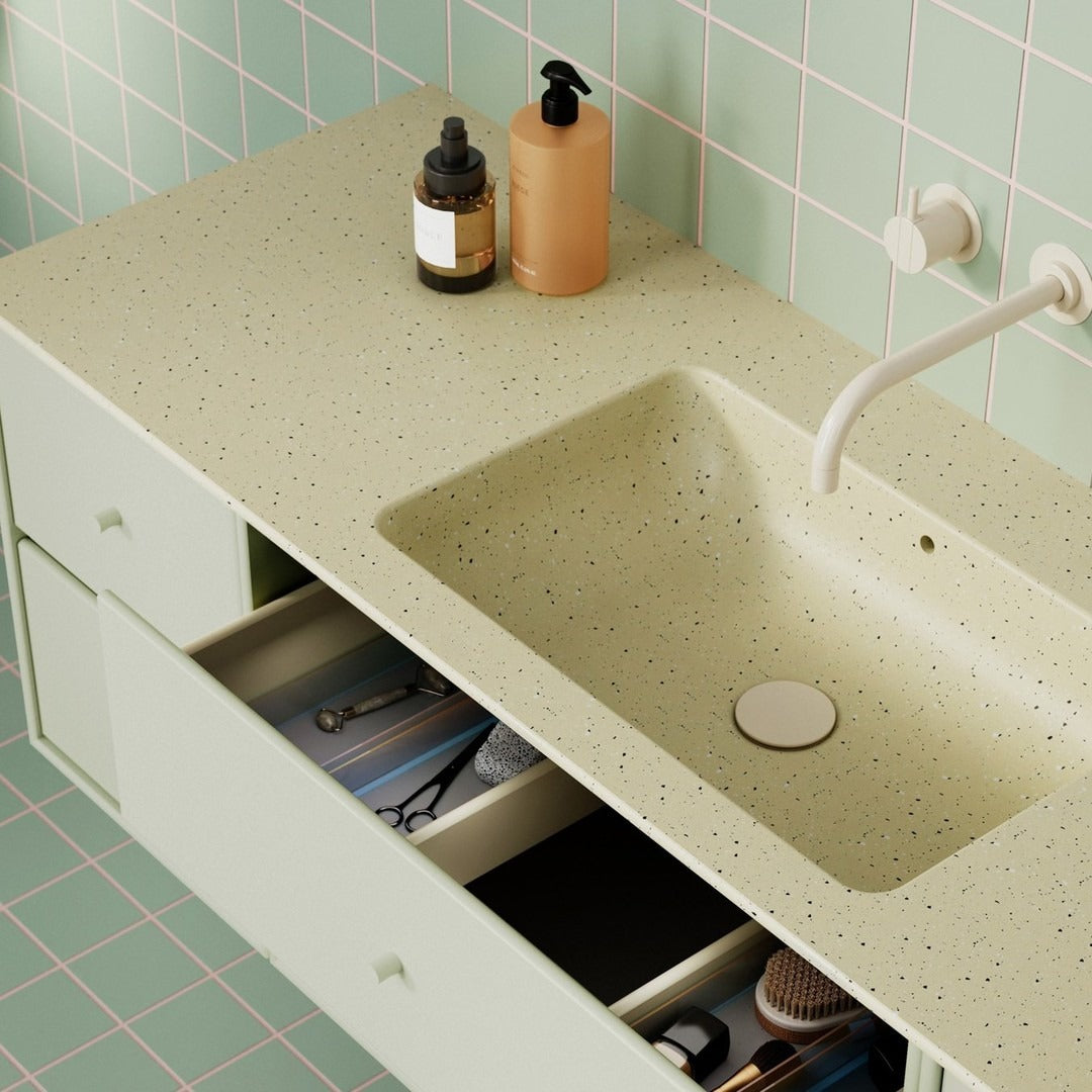 Light green speckled countertop with pale green drawers against soft mint tiled wall. Modern, minimalist bathroom design.