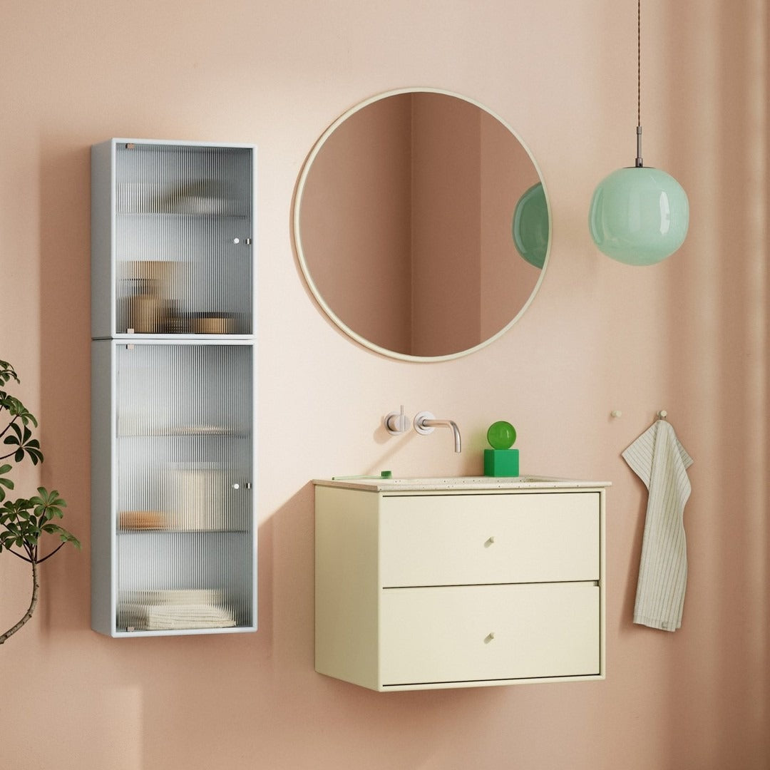 "Light pastel pink wall with cream cabinetry, silver shelving, and mint green pendant light, featuring soft curves."