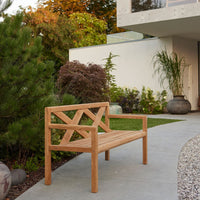 Natural light wood bench with a geometric pattern, surrounded by lush greenery and a neutral stone path.