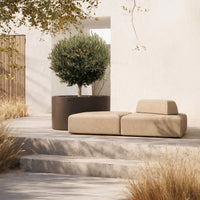 Beige modular sofa on a light stone patio, surrounded by greenery and earthy tones. Soft, modern design.