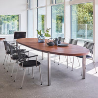 Modern wooden table with a rich brown finish, surrounded by black striped chairs, set in a bright, airy space.