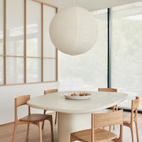 Round white pendant light above a soft beige table surrounded by light wooden chairs in a bright, airy room.