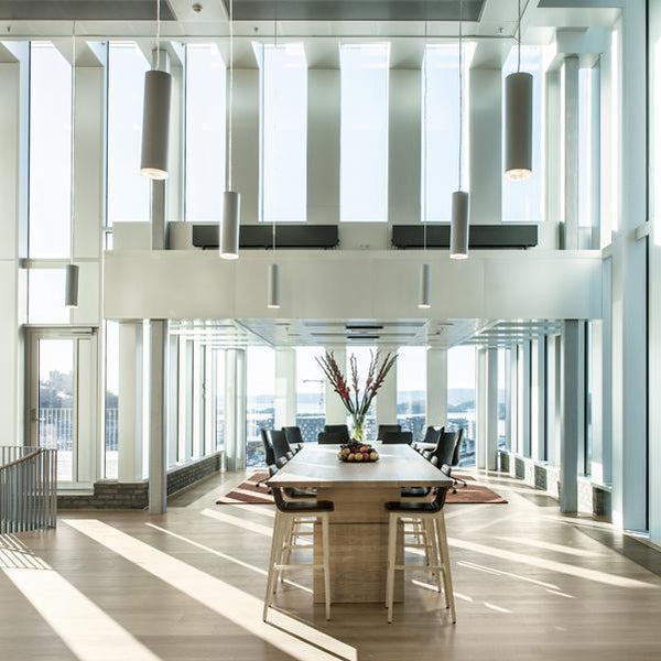 Modern dining area featuring light wooden table, black chair accents, and bright white walls with large windows.