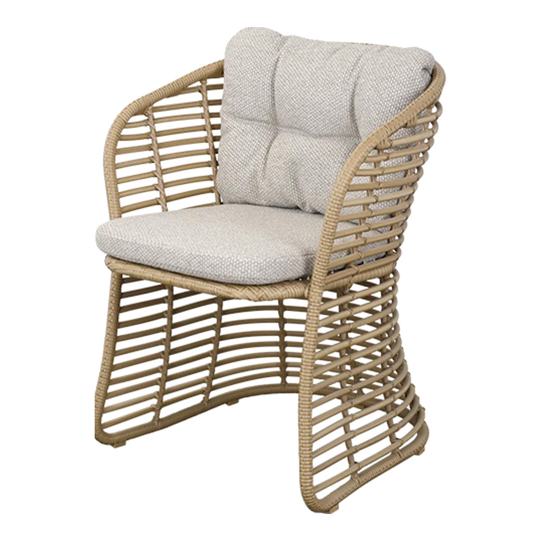 Light beige cushion on a woven natural rattan chair with a modern, curved design and open pattern. Perfect for outdoor decor.