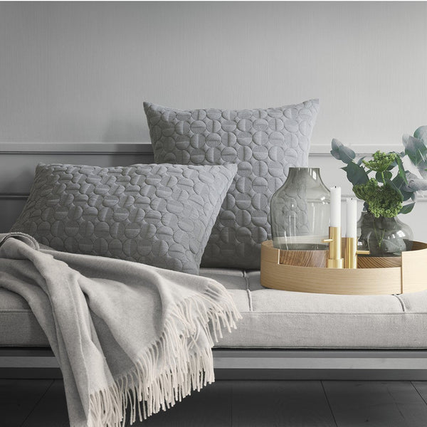 Gray textured throw pillows with a subtle pattern, cozy beige throw, and a golden tray against a neutral backdrop.