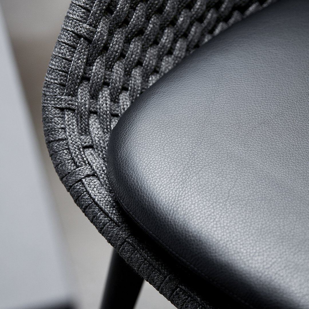 Close-up of a chair with woven backrest and leather seat.