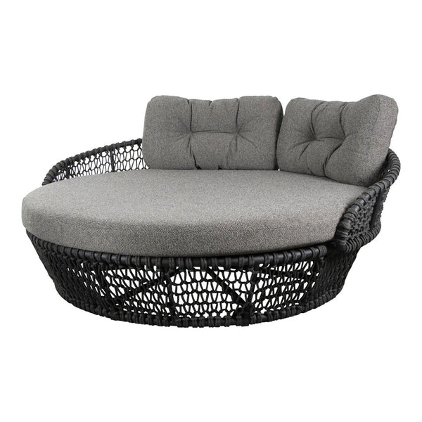 Round wicker daybed with black woven base and plush gray cushions, featuring tufted design for added comfort.