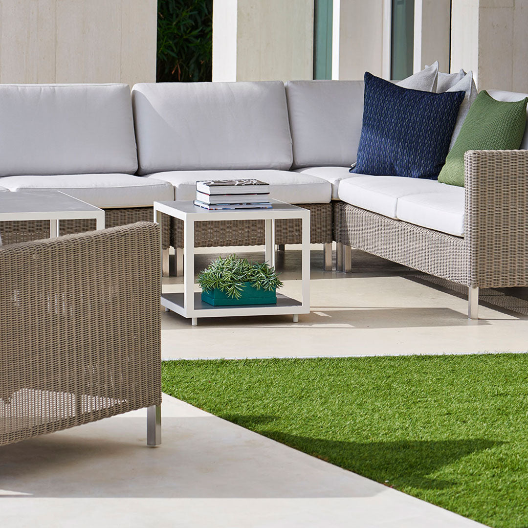 Modern outdoor seating in neutral tones with blue and green accent pillows, woven texture, and clean white table.