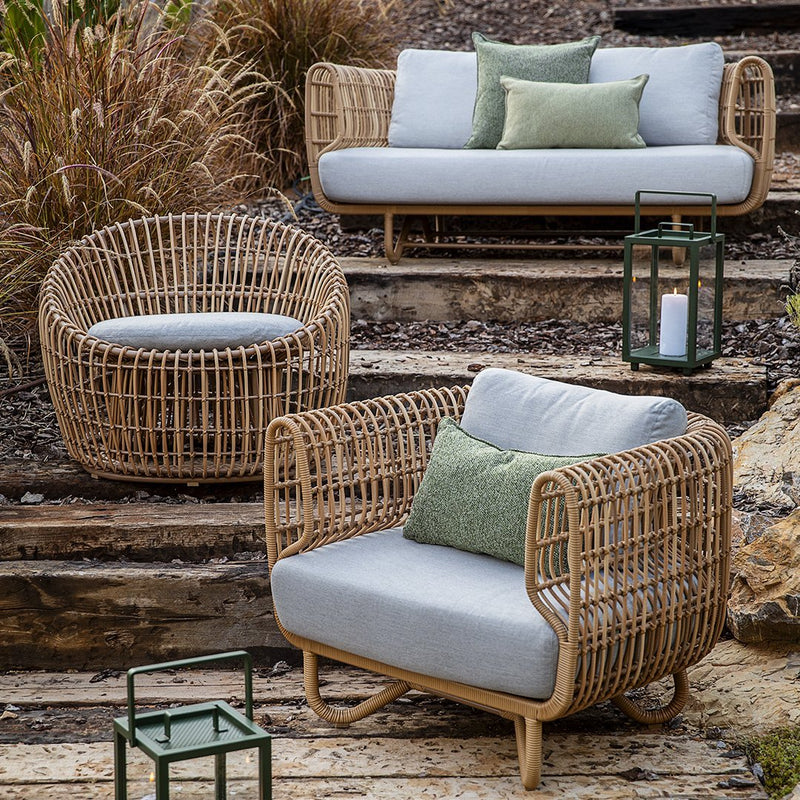 Natural wicker furniture in soft grey cushions with leafy green accents, perfect for outdoor relaxation.