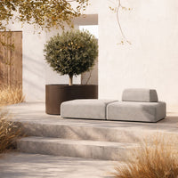 Gray modular sofa with a smooth texture, complemented by earthy tones of surrounding patio and decorative greenery.