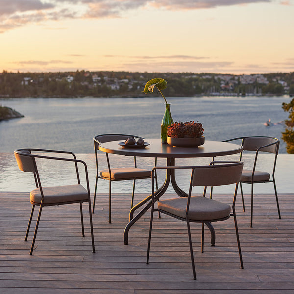 Modern outdoor dining set featuring a round wooden table and four black metal chairs with light gray cushions.