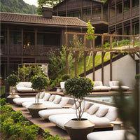 Stylish white lounge chairs with green foliage and wooden accents, set in a serene, natural landscape.