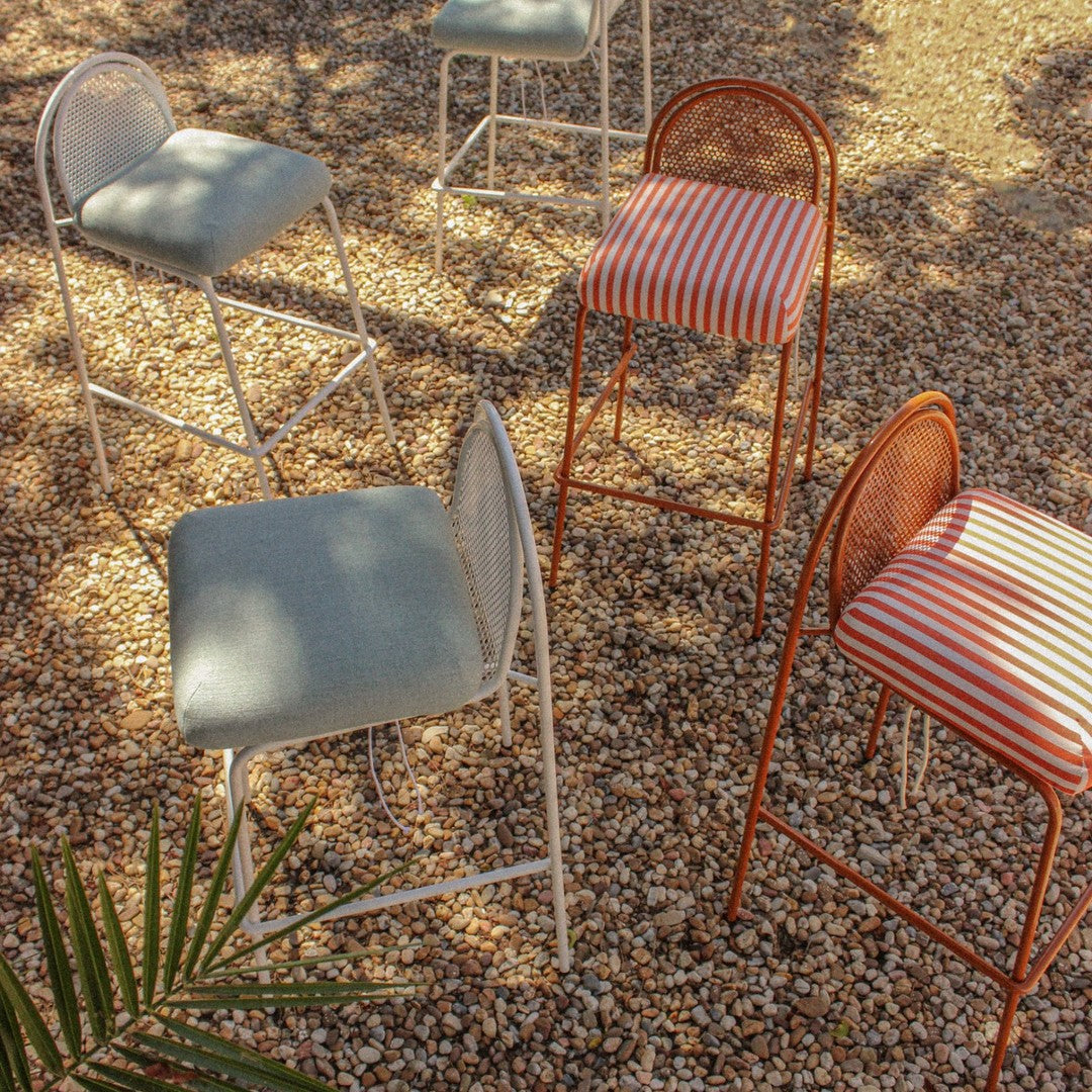 Colorful chairs featuring light blue, red-striped, and natural woven patterns on a textured gravel surface.