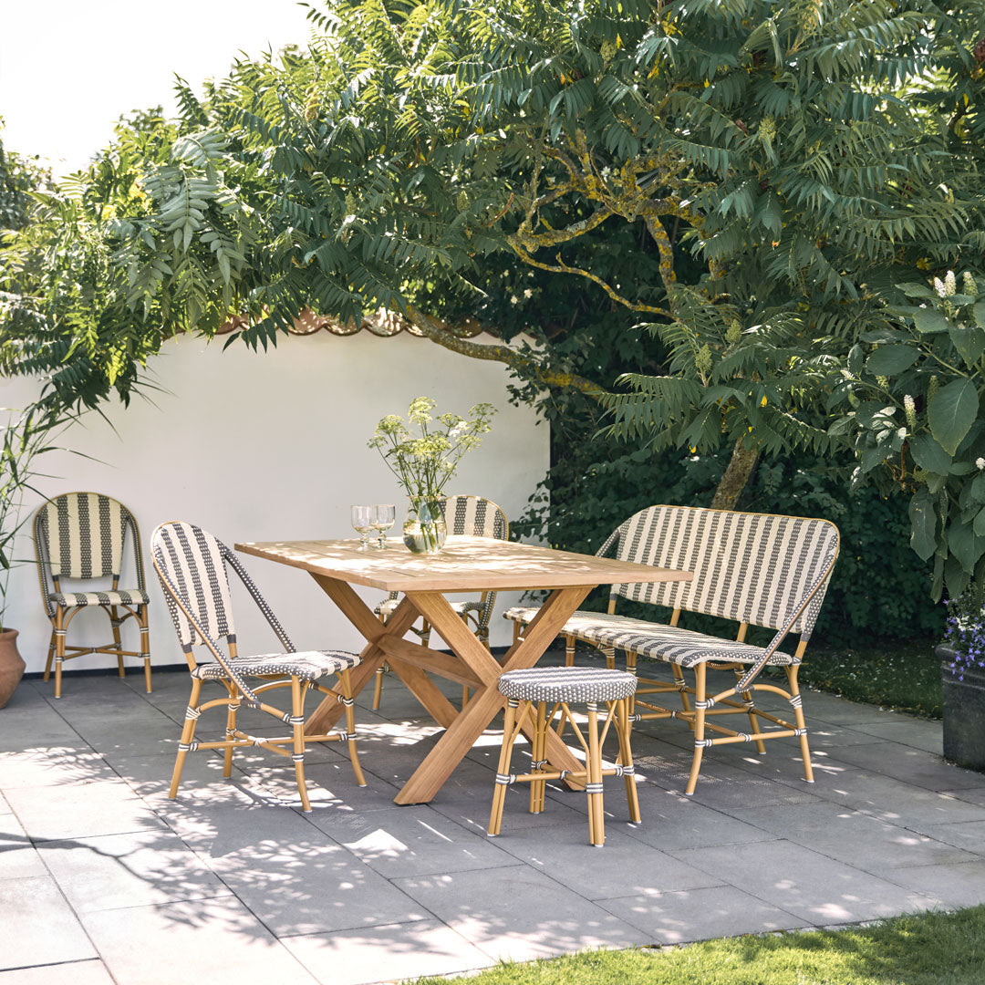 "Outdoor dining set with striped black and white cushions on natural wood frame, surrounded by lush green foliage."