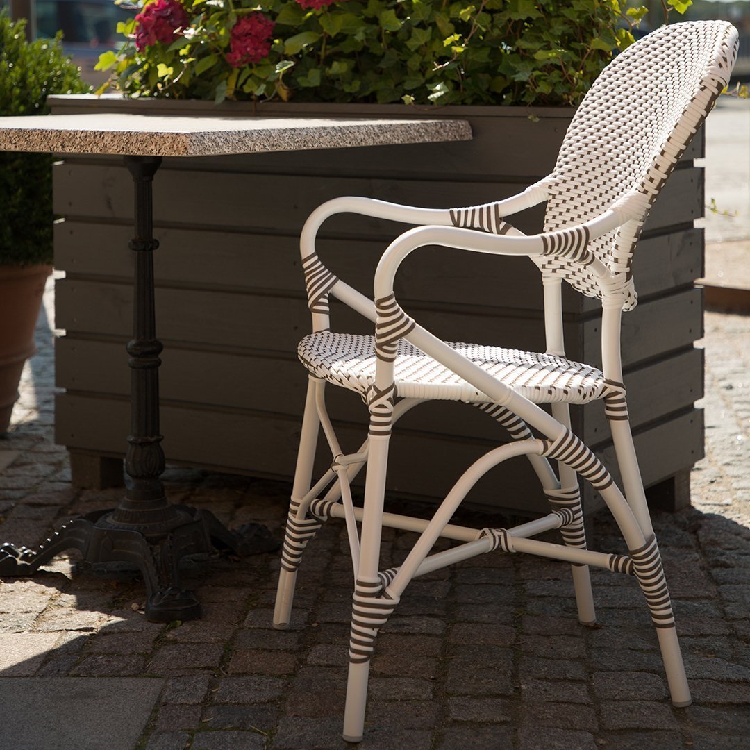 "White and brown striped wicker chair with elegant patterns beside a textured stone table and greenery."