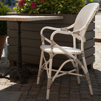 "White and brown striped wicker chair with elegant patterns beside a textured stone table and greenery."
