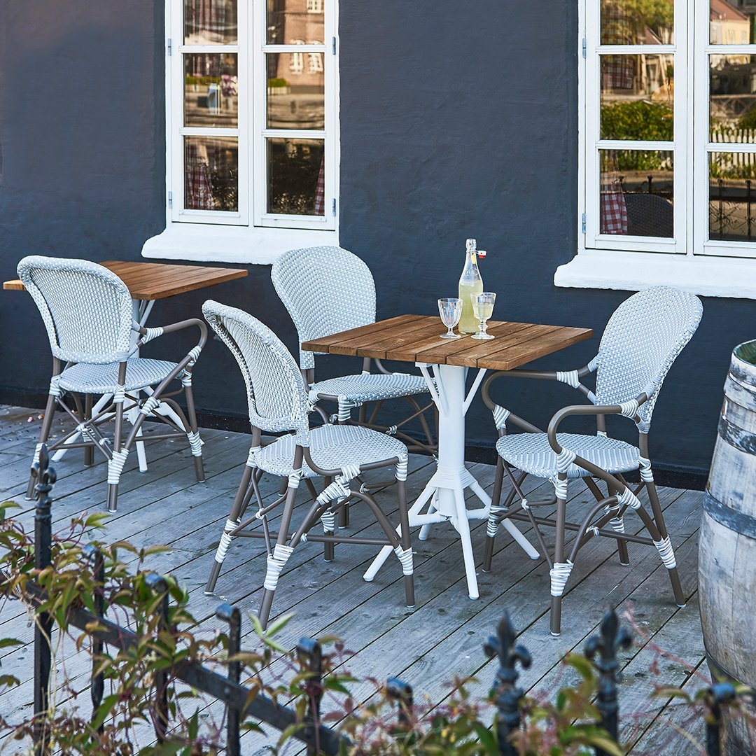 White and beige bistro chairs with wooden table, set against a dark gray wall, ideal for outdoor dining.