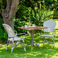 Gray wicker chairs with textured patterns, natural wood table, and white mugs in a lush green garden setting.